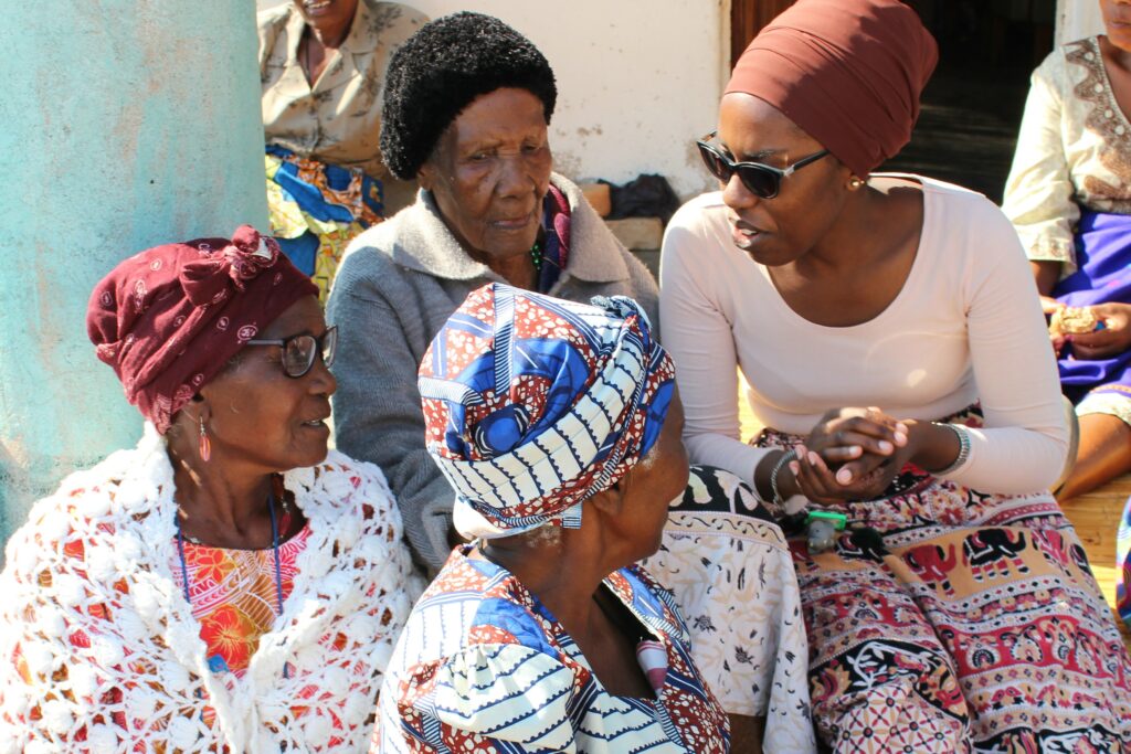 young woman greeting three elderly women with hands cupped